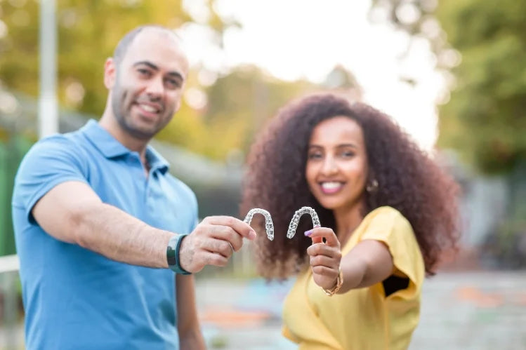 A couple smiling and holding transparent clear aligners in their hands