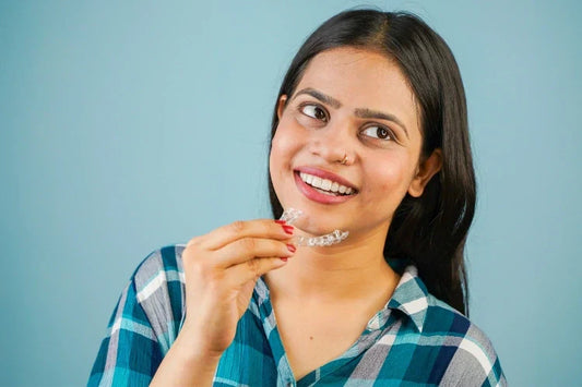 A girl is holding a clear aligner while smiling with perfect teeth