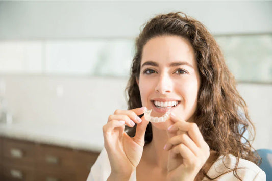 A girl holding clear aligners and smiling.