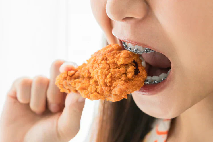 An image of a girl eating fried chicken with braces