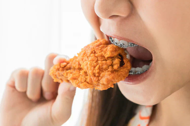 An image of a girl eating fried chicken with braces