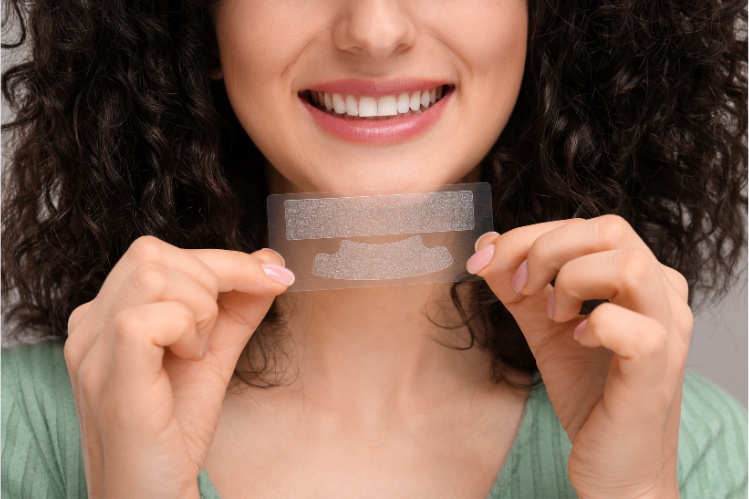 A woman is holding teeth whitening strips