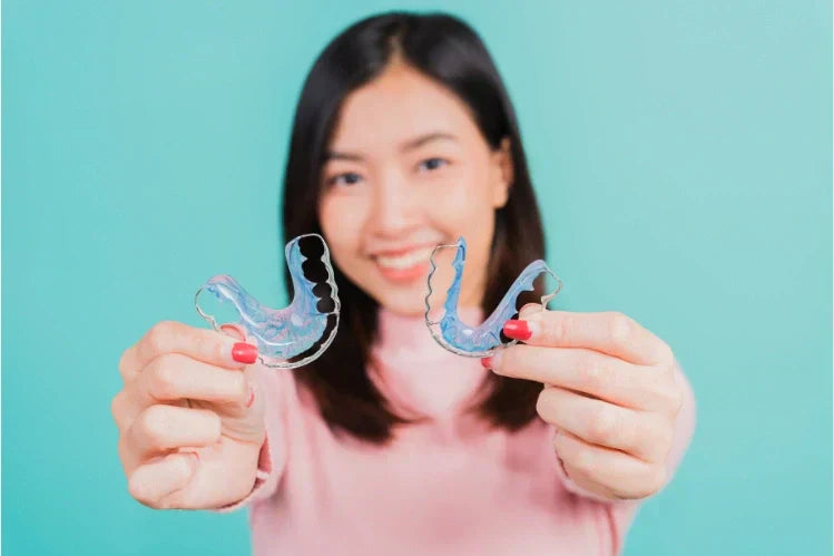 A woman holding up two Hawley retainers and smiling.